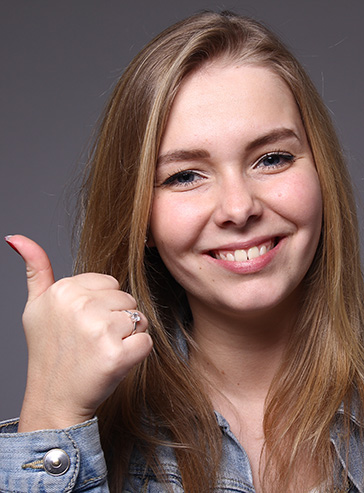 Junge Frau mit langen braunen Haaren zeigt Daumen nach oben und freut sich