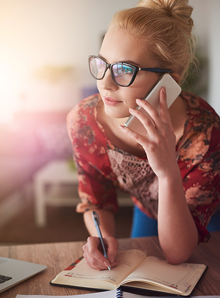 Junge Frau mit Handy am Ohr schreibt sich Notizen in ihren Kalender